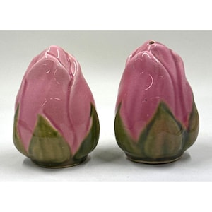 May include: A pair of ceramic salt and pepper shakers shaped like pink flower buds with green bases. The shakers have a glossy finish and are designed to resemble a tulip or similar flower.