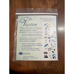 Puede incluir: Un paquete de plástico sellado que contiene formas recortadas de álbumes de recortes con un tema de vacaciones. El paquete incluye varias formas como palmeras, una tienda de campaña y un coche. El texto dice "Vacation" y "Creative Memories Collection."