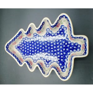 May include: A ceramic dish shaped like a Christmas tree with a cream-colored base. The surface features a dense pattern of small blue floral motifs and a border of blue circles with red and green accents along the scalloped edges of the dish.