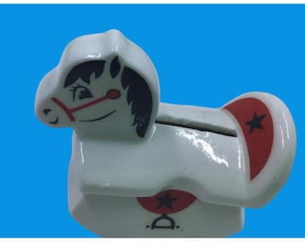 Hucha vintage de cerámica con forma de caballito mecedor, color blanco con detalles de estrellas rojas y negras, ideal para coleccionistas.