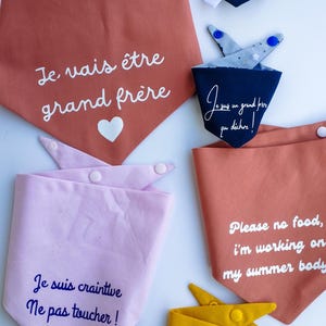 Puede incluir: Cinco bandanas de tela con diferentes colores y diseños. Las bandanas tienen texto en francés e inglés. El texto en las bandanas incluye "Je vais être grand frère", "Je suis craintive Ne pas toucher!" y "Please no food, I'm working on my summer body".