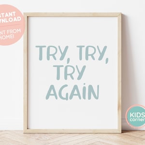 Könnte beinhalten: Ein gerahmter Druck mit hellblauem Hintergrund und dem Text "TRY, TRY, TRY AGAIN" in einer verspielten Schriftart. Der Druck ist in einem Holzrahmen und liegt auf einem Holzboden.