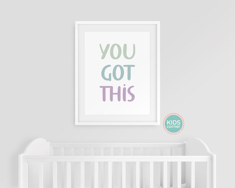 May include: White framed print with the text "YOU GOT THIS" in pastel green, blue, and purple lettering. The print is hanging on a white wall above a white crib.