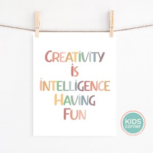 Op de afbeelding: Een printable wandposter met de tekst "Creativity is intelligence having fun" in kleurrijke letters. De poster hangt aan een witte muur met twee houten wasknijpers.