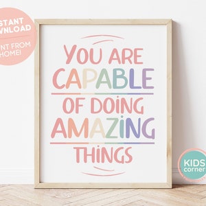 May include: A printable poster with the text "You are capable of doing amazing things" in rainbow colors. The poster is framed in a light wood frame and is sitting on a wooden floor.