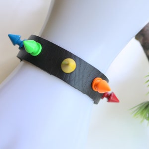 May include: A black leather bracelet with colourful spikes. The spikes are blue, green, yellow, orange and red.