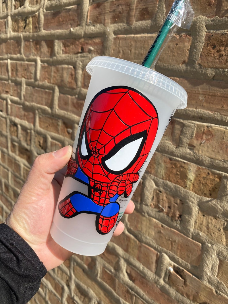 Puede incluir: Un vaso reutilizable de pl&aacute;stico transparente con una imagen de dibujos animados de Spiderman en rojo y azul. El vaso tiene una tapa negra y una pajita verde.