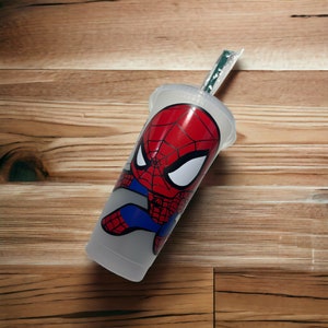 Puede incluir: Un vaso de pl&aacute;stico transparente con un dise&ntilde;o de Spiderman rojo y azul. El vaso tiene una pajita y est&aacute; sobre una superficie de madera.