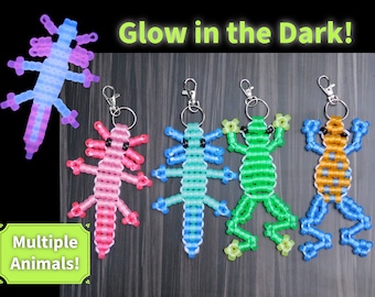 Può includere: Quattro portachiavi di animali in perline che brillano al buio. I portachiavi hanno la forma di un axolotl, una rana e due tipi diversi di salamandre. L'axolotl è rosa, la rana è verde e le salamandre sono blu e arancioni.
