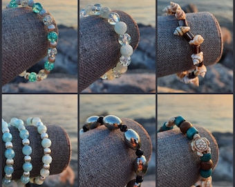 May include: Six different bracelets made with various materials, including shells, beads, and metal. The bracelets are displayed on a textured surface.