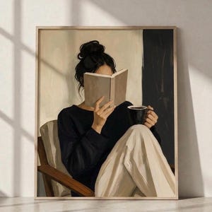 Könnte beinhalten: Ein gerahmter Wandkunstdruck, der eine Person mit dunklem Haar im Dutt zeigt, die in einem Holzstuhl sitzt. Die Person trägt ein schwarzes Langarmshirt und eine helle Hose, hält ein offenes Buch vor das Gesicht und eine schwarze Tasse in der Hand.