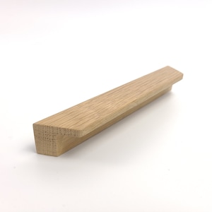 May include: A light-colored, rectangular wooden cabinet pull with a beveled edge. The wood grain is visible, and the pull is set against a white background. This is a furniture hardware component.