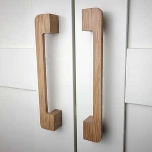 May include: Two wooden cabinet pulls with a rectangular shape and a rounded top and bottom. The pulls are a light brown color and have a smooth finish.