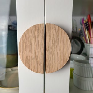 May include: Two half-circle wooden cabinet door pulls with a light wood grain finish.