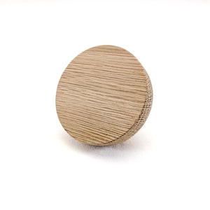 May include: A wooden cabinet knob with a light brown, natural wood grain finish. The knob is round with a slightly flattened top and a textured edge. The knob is set against a white background.