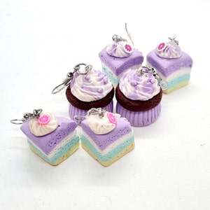 Può includere: Un set di sei orecchini a forma di cupcake e torta, di colore viola e bianco. Gli orecchini sono realizzati in pasta polimerica e hanno un aspetto realistico.