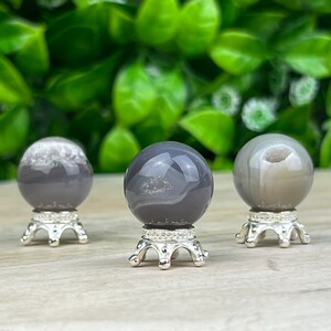 May include: Three gray agate spheres on silver stands. The spheres have a swirling pattern of gray and white.