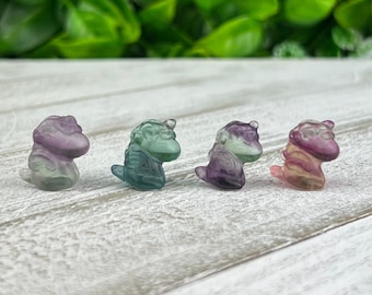May include: Four small, translucent, multi-colored unicorn figurines. The unicorns are in a row, facing the right side of the image. The unicorns are green, purple, pink, and blue.