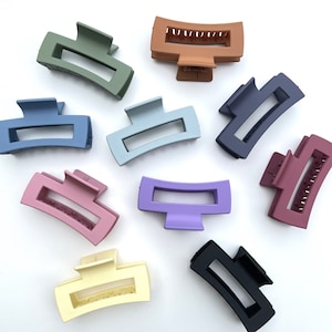 May include: Assortment of ten plastic hair clips in various colors, including black, brown, blue, green, purple, pink, and cream. The clips are all the same size and shape, with a curved design and a rectangular opening in the center.