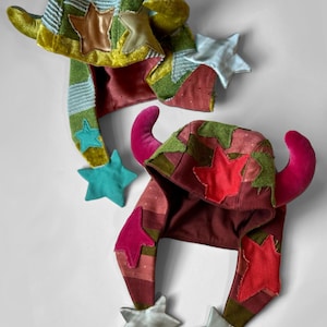 Pu&ograve; includere: Due cappelli stravaganti e colorati con dettagli a stella e corna. Uno &egrave; verde, giallo e blu con stelle marroni e azzurre. L'altro &egrave; rosso, verde e rosa con corna rosa e stelle argentate.