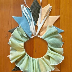May include: A green ruffled fabric collar with a white trim. The collar is attached to a set of fabric points in blue, brown, and peach.