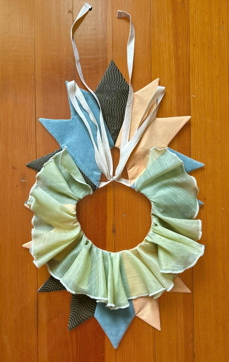 May include: A green ruffled fabric collar with a white trim. The collar is attached to a set of fabric points in blue, brown, and peach.