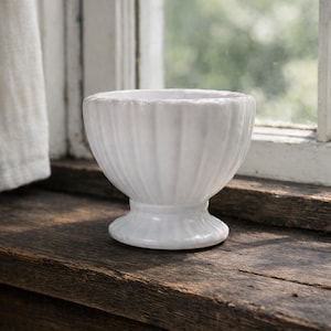 May include: A white ceramic mug with a black handle and the text "But First, Coffee" in a black, handwritten-style font. The mug is on a white surface.