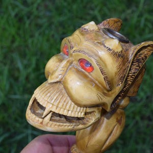May include: A carved wooden pipe in the shape of a gargoyle with red eyes. The pipe has a hole in the top for tobacco.
