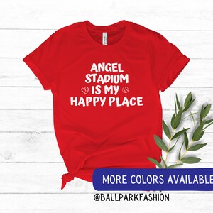 May include: Red t-shirt with white text that reads "Angel Stadium is my happy place" with a heart and baseball graphic.  More colors available @ballparkfashion