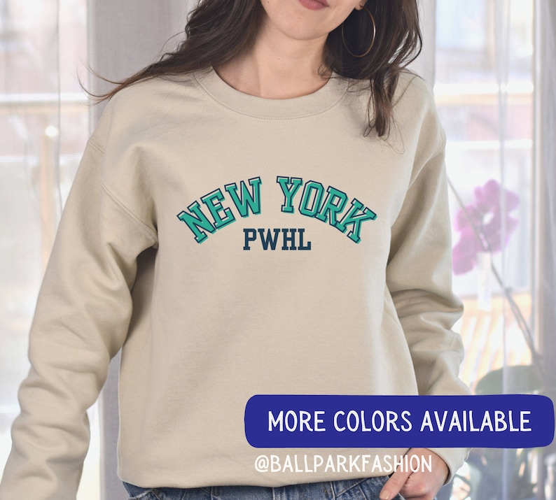 May include: A beige sweatshirt with a teal blue and navy blue graphic that says "NEW YORK PWHL" on the front.