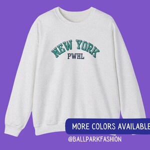 May include: A heather grey sweatshirt with a green and white "NEW YORK" graphic with the text "PWHL" underneath. The sweatshirt is a long-sleeved crew neck style.