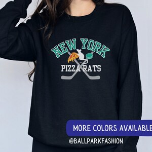 May include: Black sweatshirt with a green and white graphic design that says "New York Pizza Rats" with a rat holding a slice of pizza and a hockey puck. The graphic also includes two crossed hockey sticks.