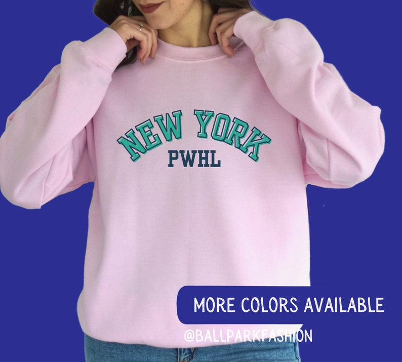 May include: Pink sweatshirt with a teal blue and navy blue graphic that says "NEW YORK PWHL" on the front.