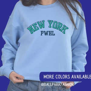 May include: Light blue sweatshirt with a green and white "NEW YORK PWHL" graphic.