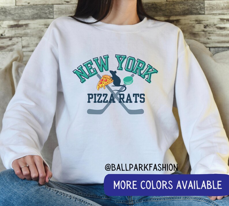 May include: White sweatshirt with a graphic design featuring the words "New York Pizza Rats" in teal and black lettering. The graphic also includes a pizza slice, a rat, and two hockey sticks.