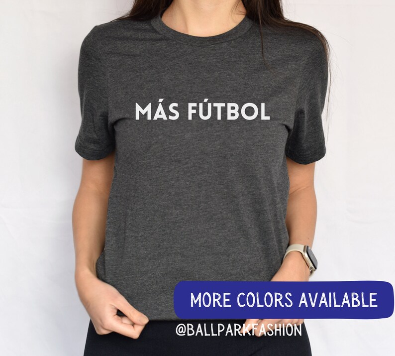 Puede incluir: Una camiseta gris oscuro con el texto "M&Aacute;S F&Uacute;TBOL" impreso en blanco en la parte delantera. El texto est&aacute; centrado en la camiseta. La camiseta est&aacute; hecha de un material suave y c&oacute;modo y es perfecta para el uso diario.