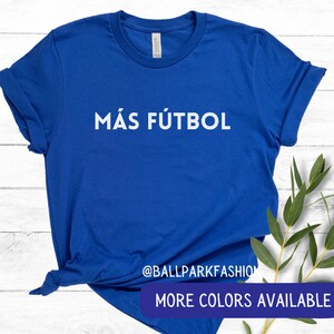 Puede incluir: Una camiseta azul real con el texto "M&Aacute;S F&Uacute;TBOL" en letras blancas. La camiseta est&aacute; hecha de un material suave y c&oacute;modo y es perfecta para el uso diario.  @BALLPARKFASHION M&Aacute;S COLORES DISPONIBLES