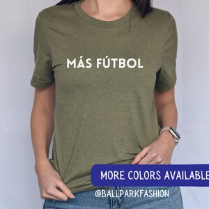Puede incluir: Una camiseta verde con el texto "M&Aacute;S F&Uacute;TBOL" en letras blancas. El texto est&aacute; centrado en la camiseta. La camiseta est&aacute; siendo usada por una persona. La imagen tambi&eacute;n incluye el texto "MORE COLORS AVAILABLE" y "@BALLPARKFASHION" en letras azules.