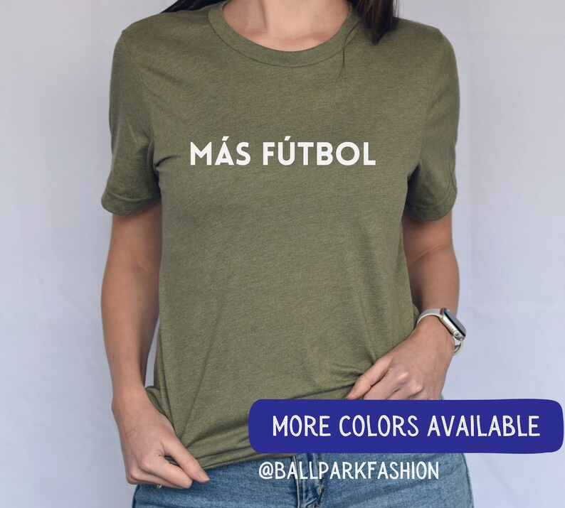 Puede incluir: Una camiseta verde con el texto "M&Aacute;S F&Uacute;TBOL" en letras blancas. El texto est&aacute; centrado en la camiseta. La camiseta est&aacute; siendo usada por una persona. La imagen tambi&eacute;n incluye el texto "MORE COLORS AVAILABLE" y "@BALLPARKFASHION" en letras azules.