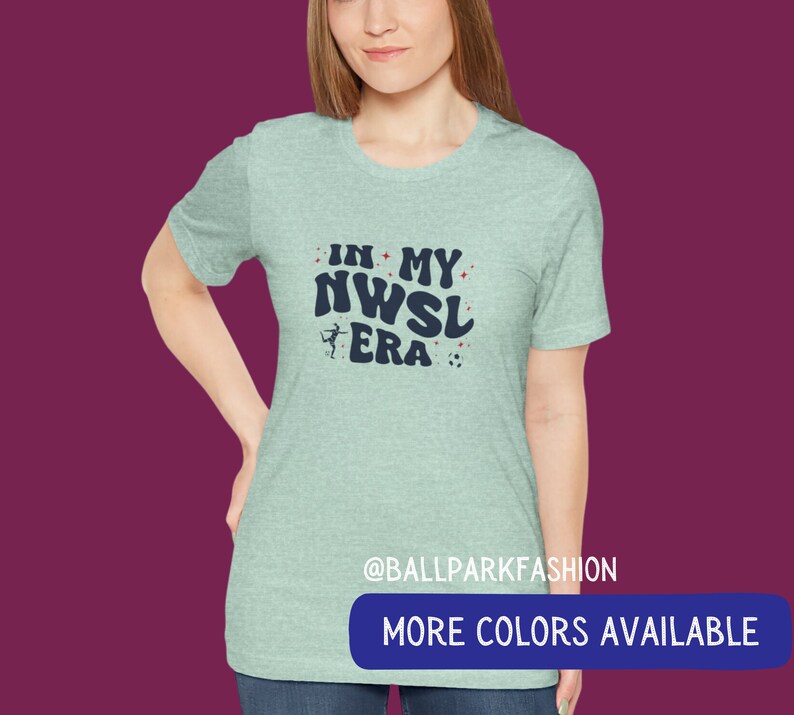Pu&ograve; includere: Una maglietta blu chiaro con il testo "In My NWSL Era" in blu navy con una stella rossa e un'immagine di pallone da calcio. Il testo &egrave; in un font retr&ograve;. La maglietta ha un collo rotondo e maniche corte. Il testo "@ballparkfashion" &egrave; in fondo alla maglietta. Il testo "Altri colori disponibili" &egrave; in un rettangolo blu in fondo all'immagine.