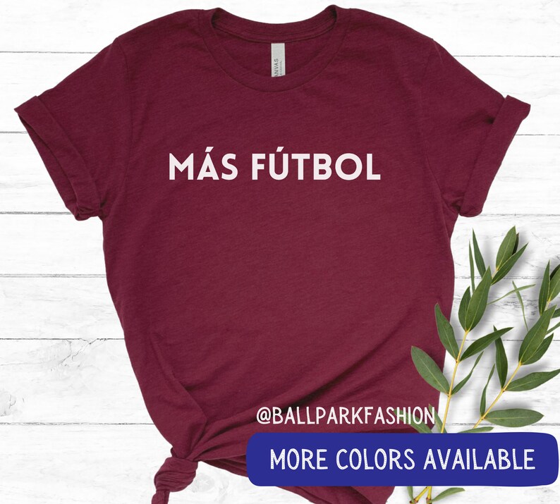 Puede incluir: Una camiseta de color burdeos con el texto "M&Aacute;S F&Uacute;TBOL" en letras blancas. La camiseta est&aacute; hecha de un material suave y c&oacute;modo y tiene un corte holgado. El texto est&aacute; centrado en la camiseta y es visible en la imagen. La camiseta est&aacute; disponible en otros colores.