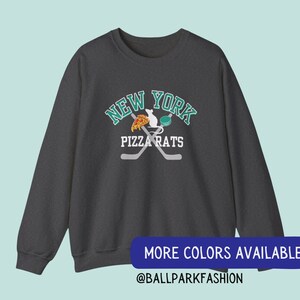 May include: Dark grey sweatshirt with a graphic of a rat eating pizza and holding a hockey stick. The graphic is surrounded by the text "New York Pizza Rats".