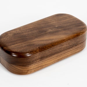May include: A wooden box with a smooth, dark brown finish. The box is oval-shaped and has a lid.