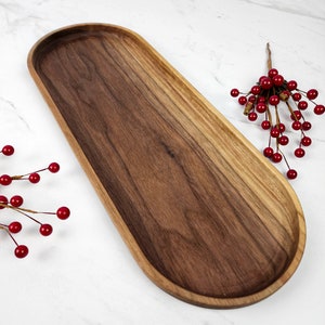 May include: An elongated, oval wooden serving tray with a dark brown interior and a lighter brown rim. The tray is made of wood and has a smooth finish. Red berries on a branch are placed on the side of the tray.
