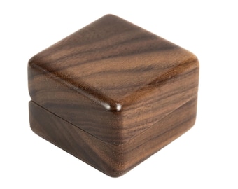 May include: A small, square wooden box with a hinged lid. The box is made of dark brown wood with a visible grain pattern. The box is likely used for jewelry or small keepsakes.