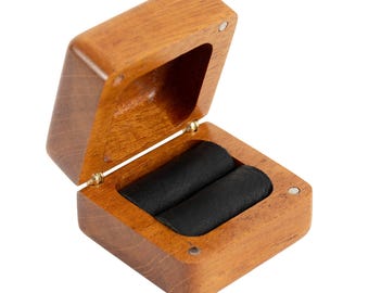 May include: Open wooden ring box with a hinged lid. The box is made of light brown wood and has a black velvet interior with two ring slots. The box is open, revealing the interior.