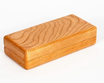 May include: A rectangular wooden box with a smooth, polished finish. The lid and base are crafted from light brown wood, showcasing a prominent, flowing natural grain pattern that runs horizontally across the top surface of the closed container.