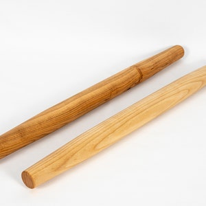 Puede incluir: Dos rodillos de amasar de madera, uno con una superficie lisa y otro con una superficie texturizada. Ambos son de madera marr&oacute;n claro.