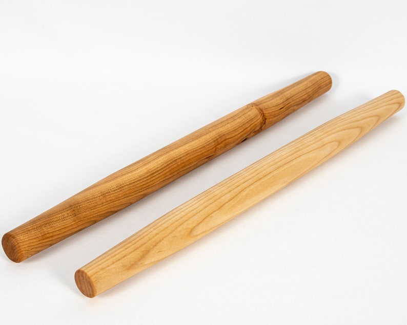 Puede incluir: Dos rodillos de amasar de madera, uno con una superficie lisa y otro con una superficie texturizada. Ambos son de madera marr&oacute;n claro.