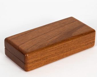May include: A rectangular wooden box with a smooth, polished finish and a visible natural grain pattern. The box features a hinged lid that sits flush with the base, creating a clean, seamless appearance with rounded edges on all sides.